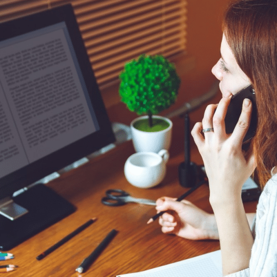 A woman on the phone and looking at a computer screen.